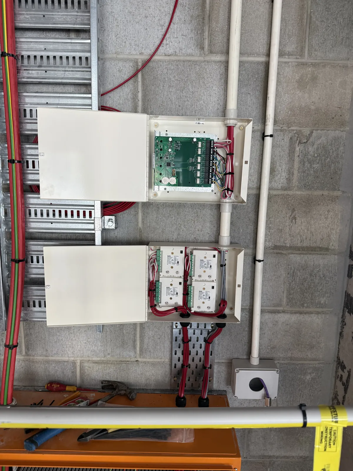 Open fire-system control cabinets with organised red cabling mounted on a block wall