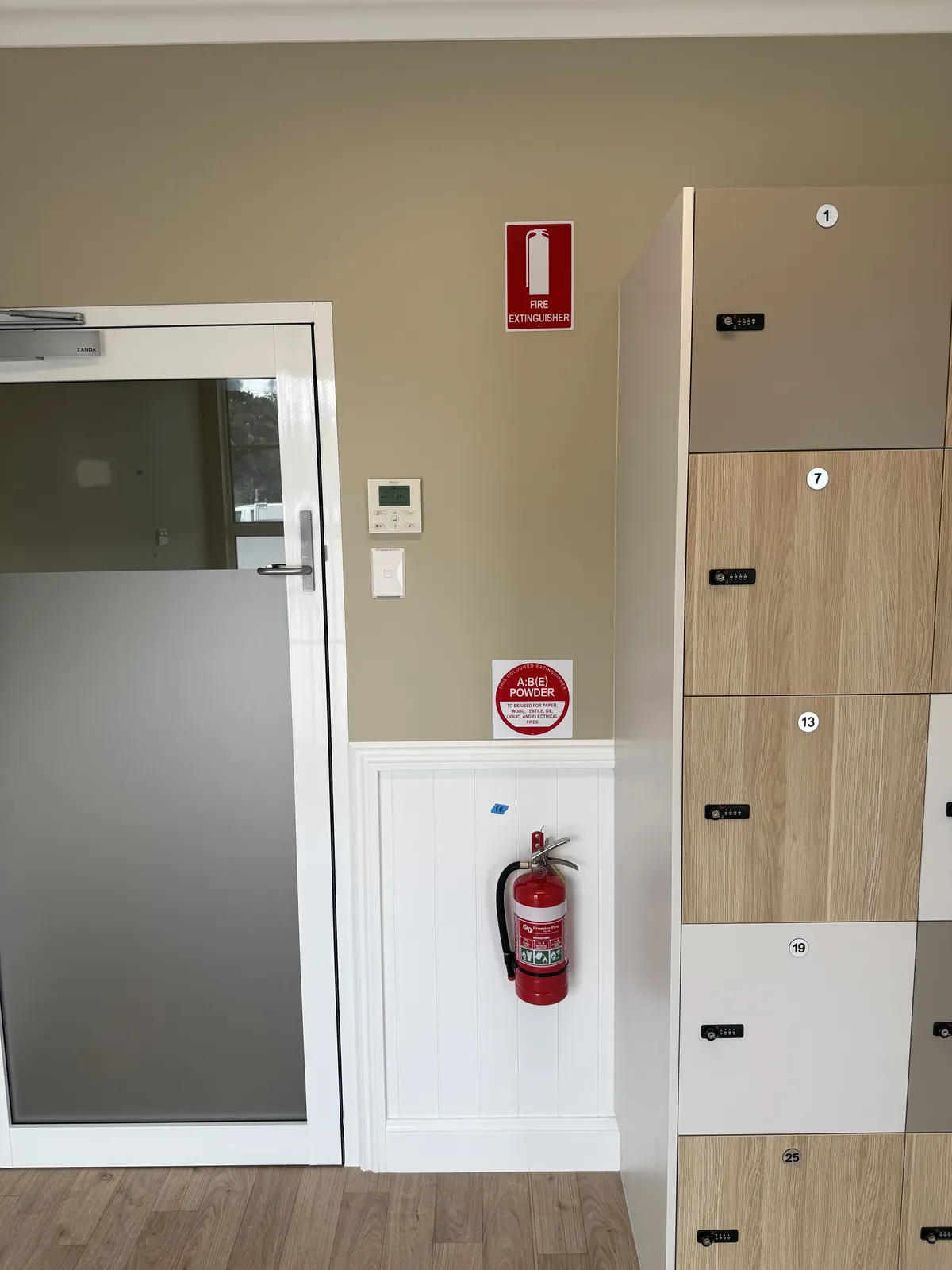 Wall-mounted red dry-powder fire extinguisher with identification signs beside numbered lockers